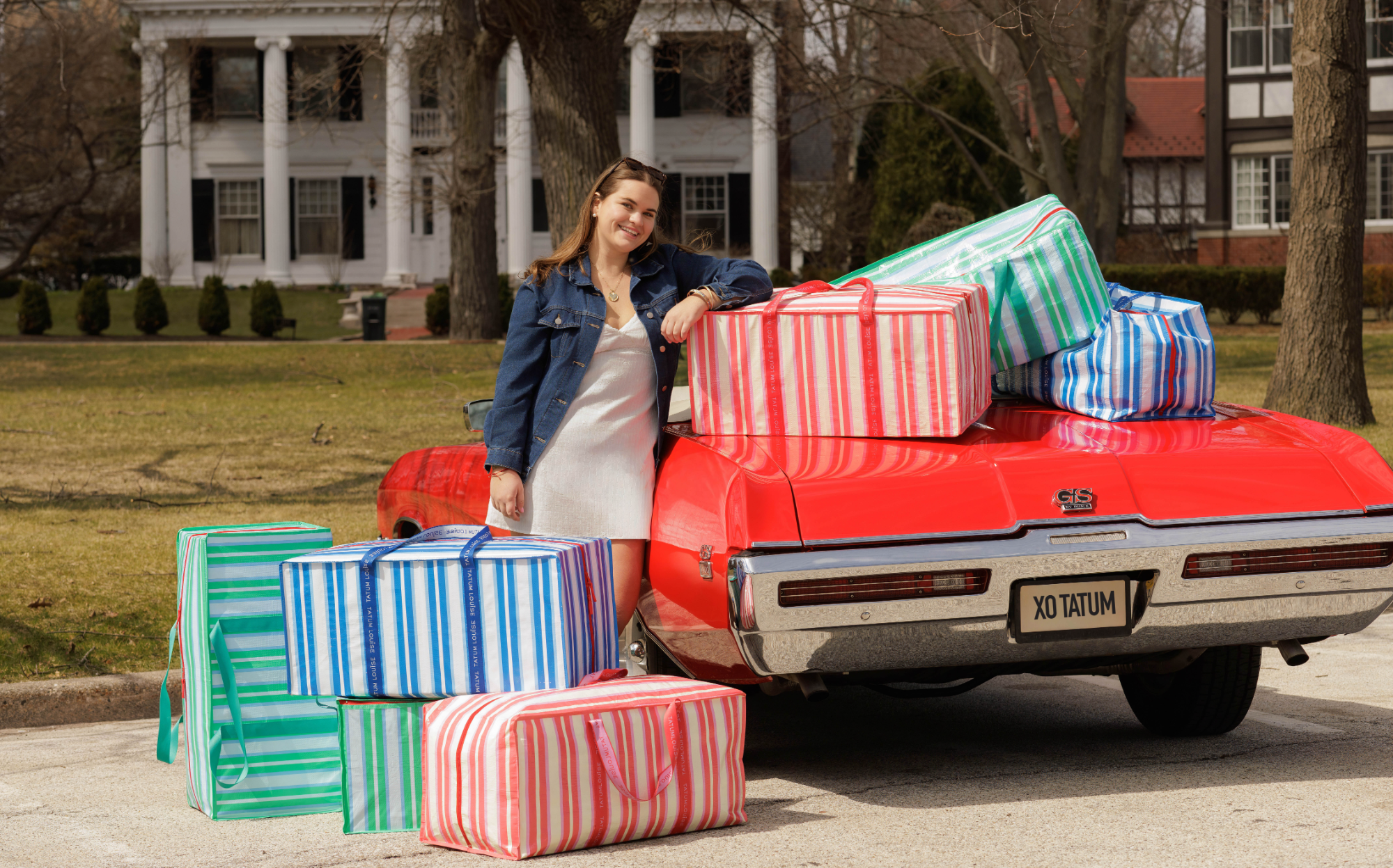 Woman with a vintage red car and colorful suitcases in front of a house.