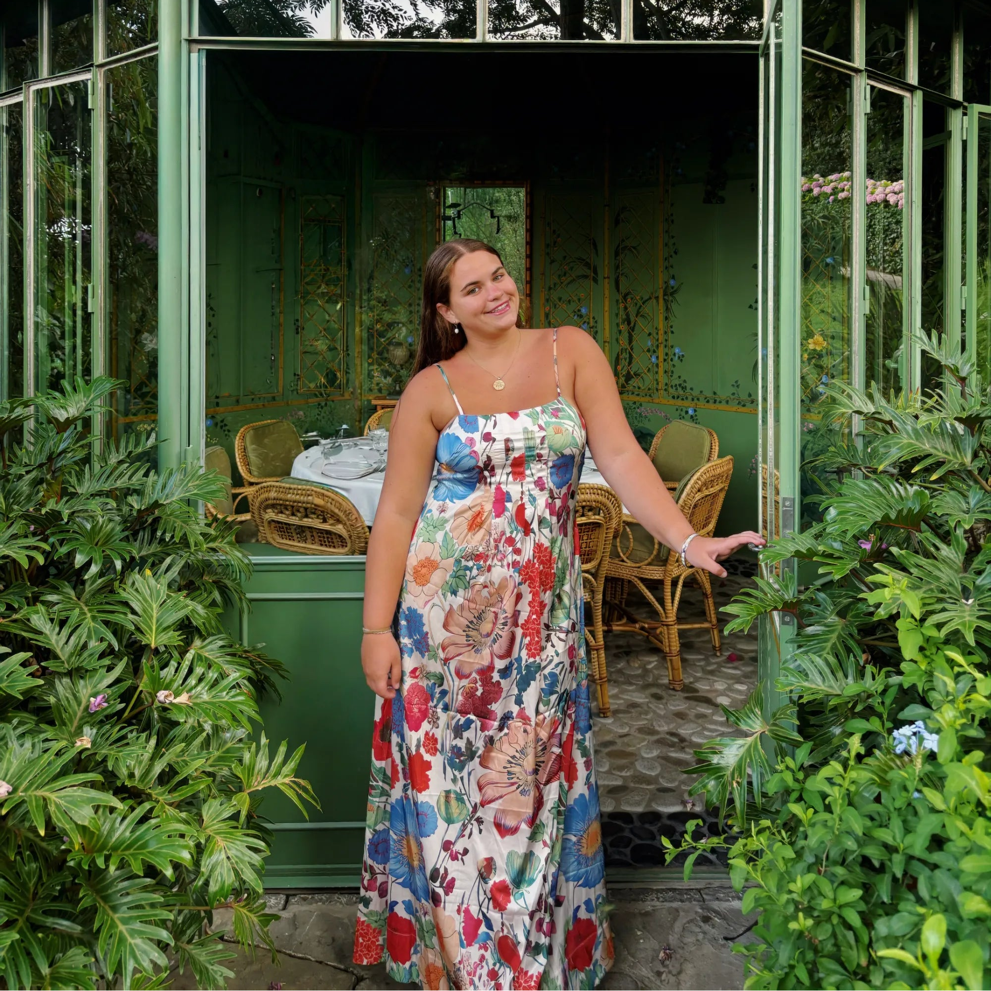 Founder of Tatum Louise in a floral dress standing in a garden with a green building in the background