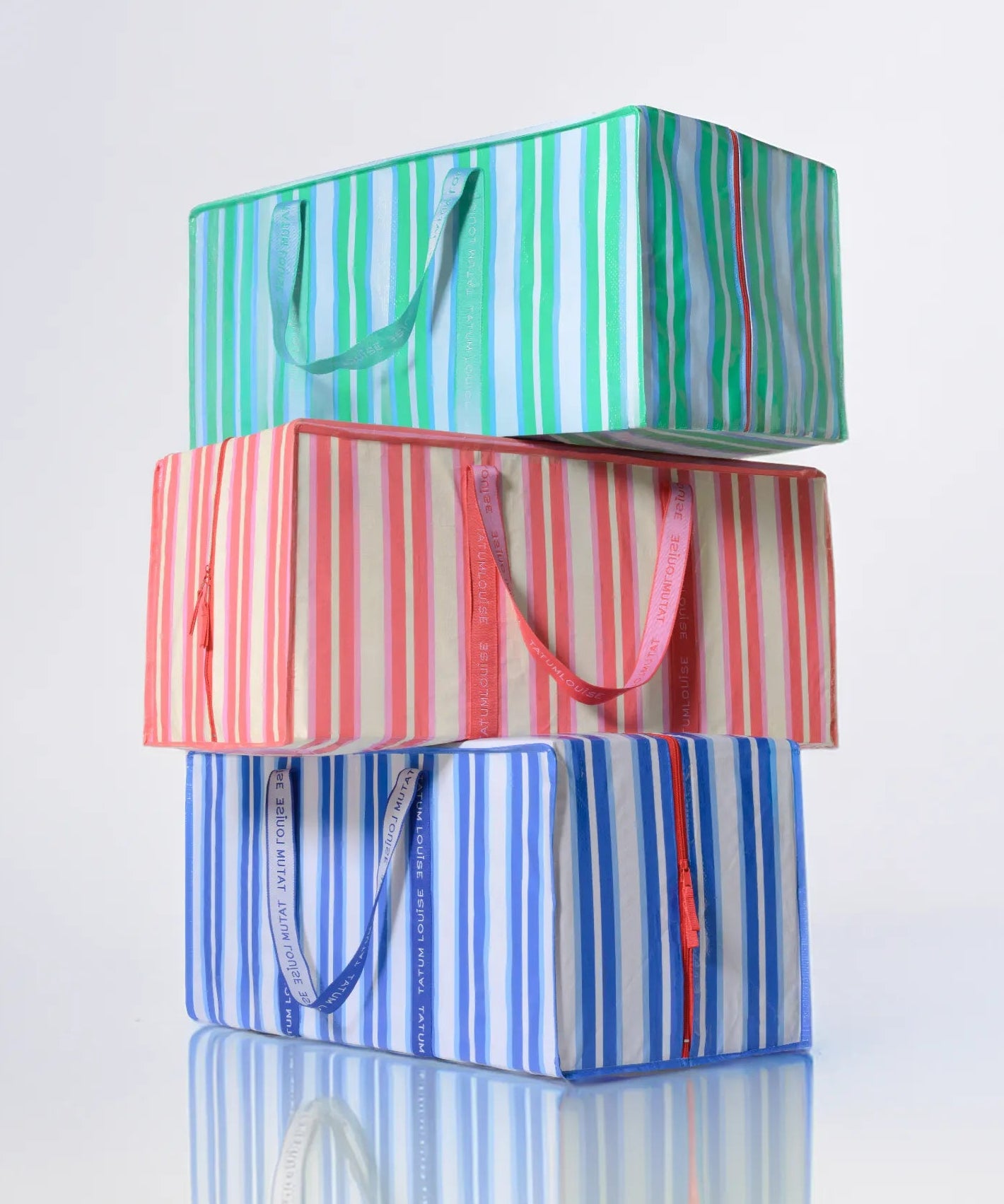 Three striped TATUM LOUISE reusable, heavy-duty moving bags stacked on a reflective surface with a light gray background
