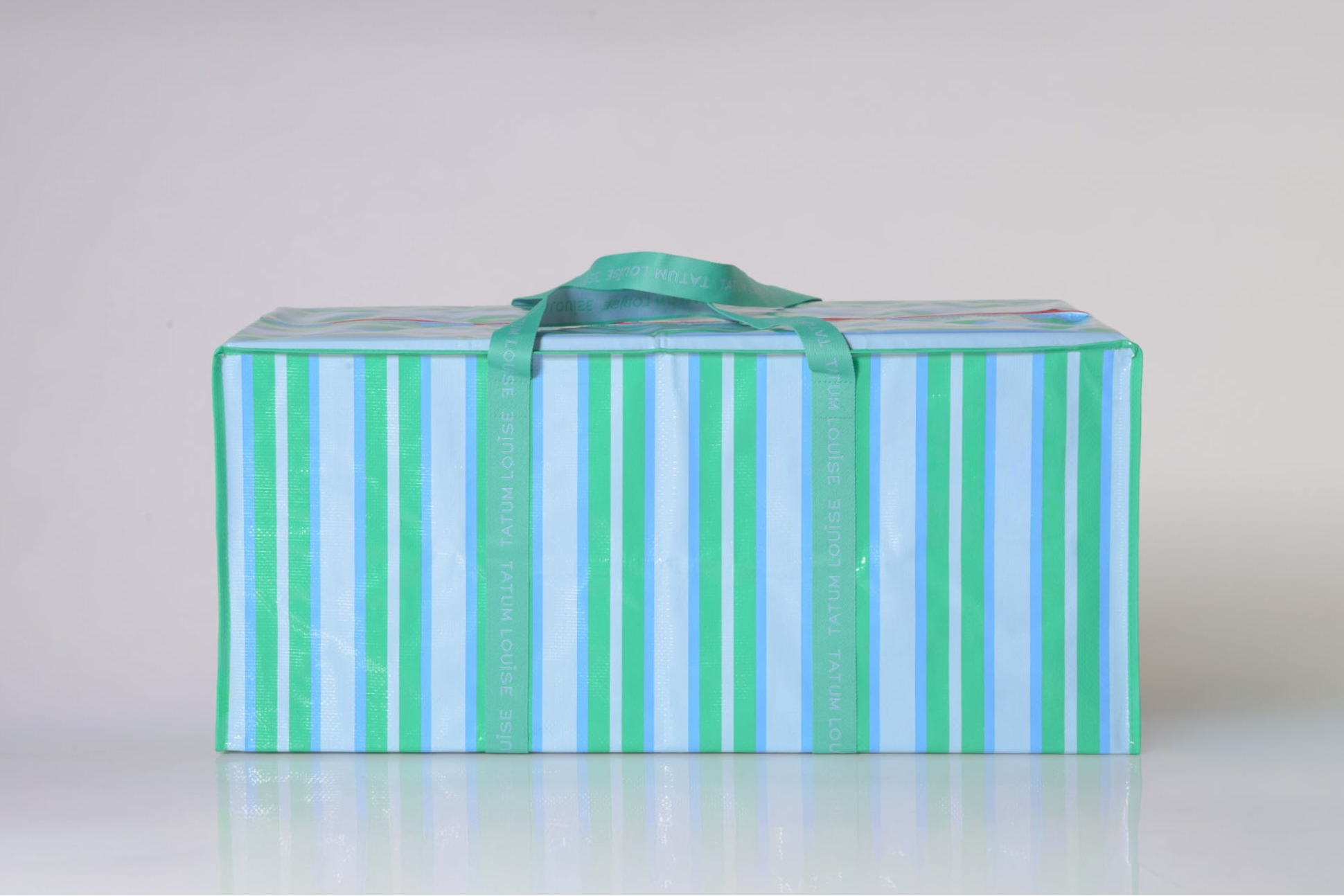 Green and blue striped moving bag with a red zipper on a white ground.
