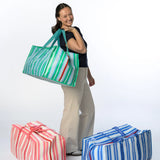 Woman holding a striped reusable moving bag for college with two additional bags on the ground against a white background.