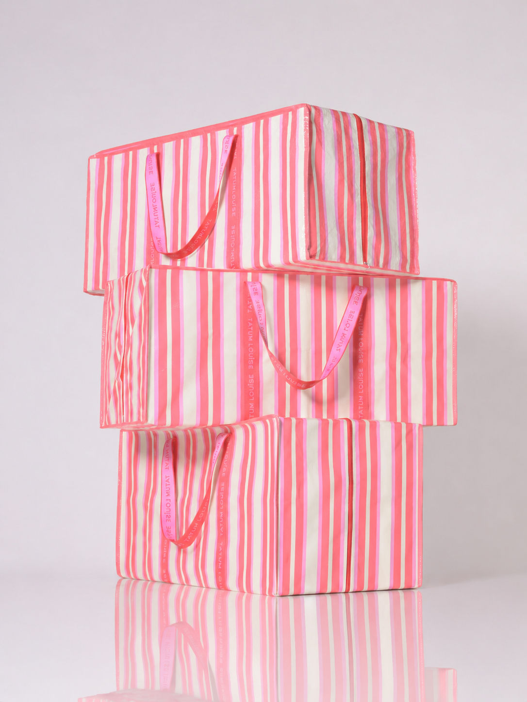 Stack of pink and white striped reusable moving bags for college on a white background